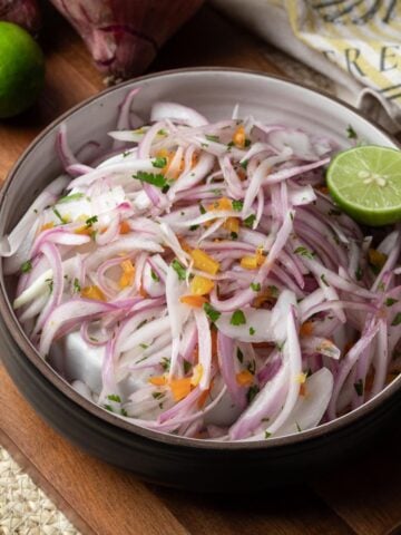 Peruvian salsa criolla in a bowl on a dark wood cutting board with whole ingredients around it.