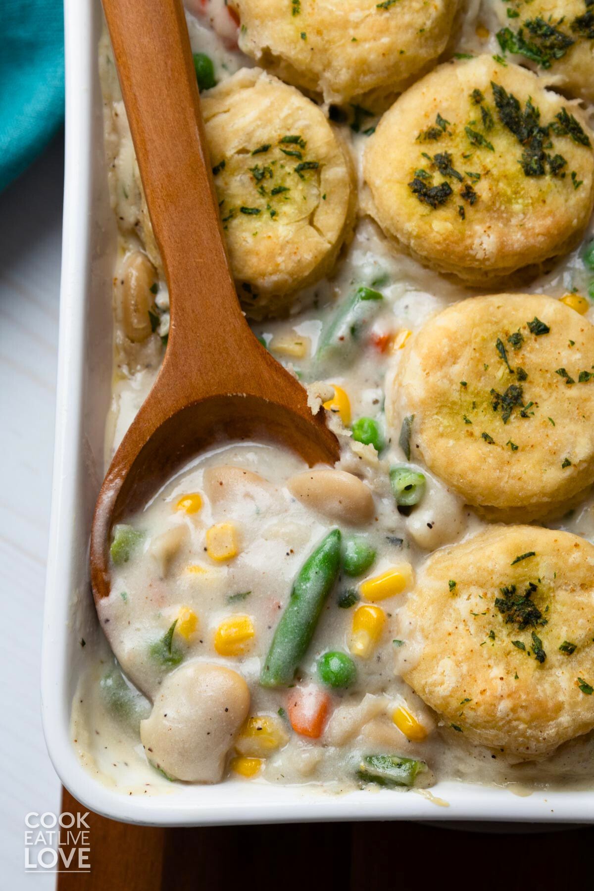 Vegan pot pie with biscuits on top and a wooden spoon scooping up some of the creamy filling.