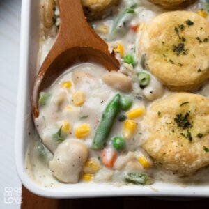 Vegan pot pie in a baking dish with a wooden spoon scooping up some of the filling.