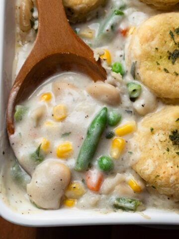 Vegan pot pie in a baking dish with a wooden spoon scooping up some of the filling.