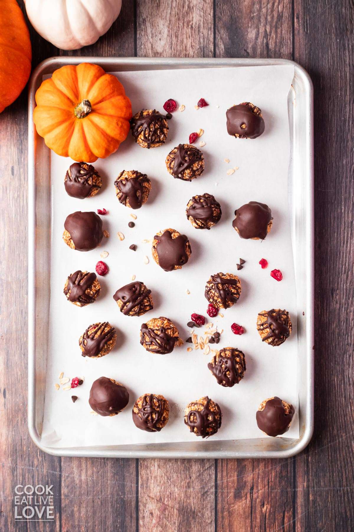 Chocolate pumpkin bites on a baking tray lined with parchment paper and a few pumpkins off to the side.