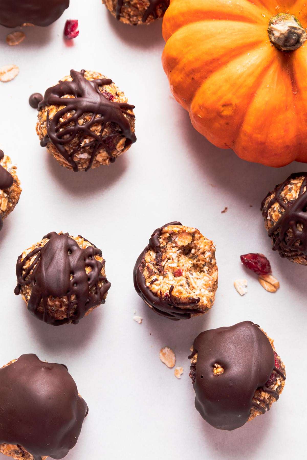 Pumpkin energy bites on a piece of parchment drizzled with chocolate and one in the middle missing a bite.