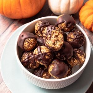 A bowl of pumpkin bites on the table with a bite missing from one and some pumpkins in the background.