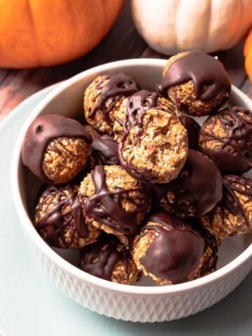 A bowl of pumpkin bites on the table with a bite missing from one and some pumpkins in the background.