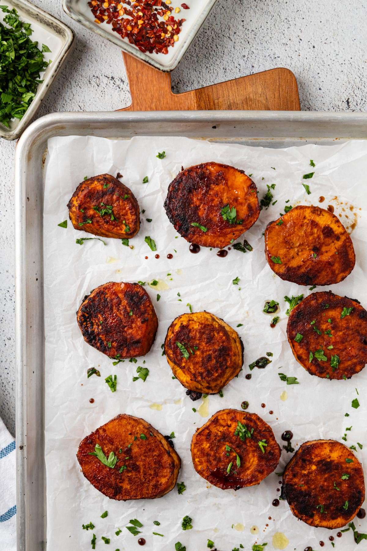 Baking pan topped with sweet potatoes and some parsley and crushed red pepper to the side.