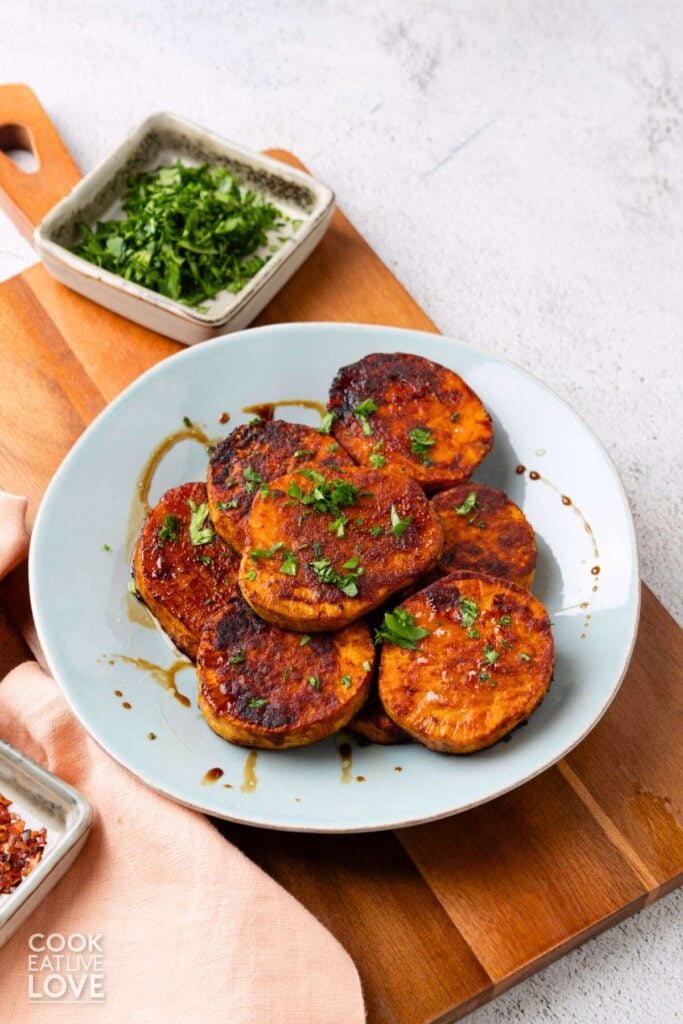 Roasted sliced sweet potatoes on a blue plate with balsamic drizzle and parsley.