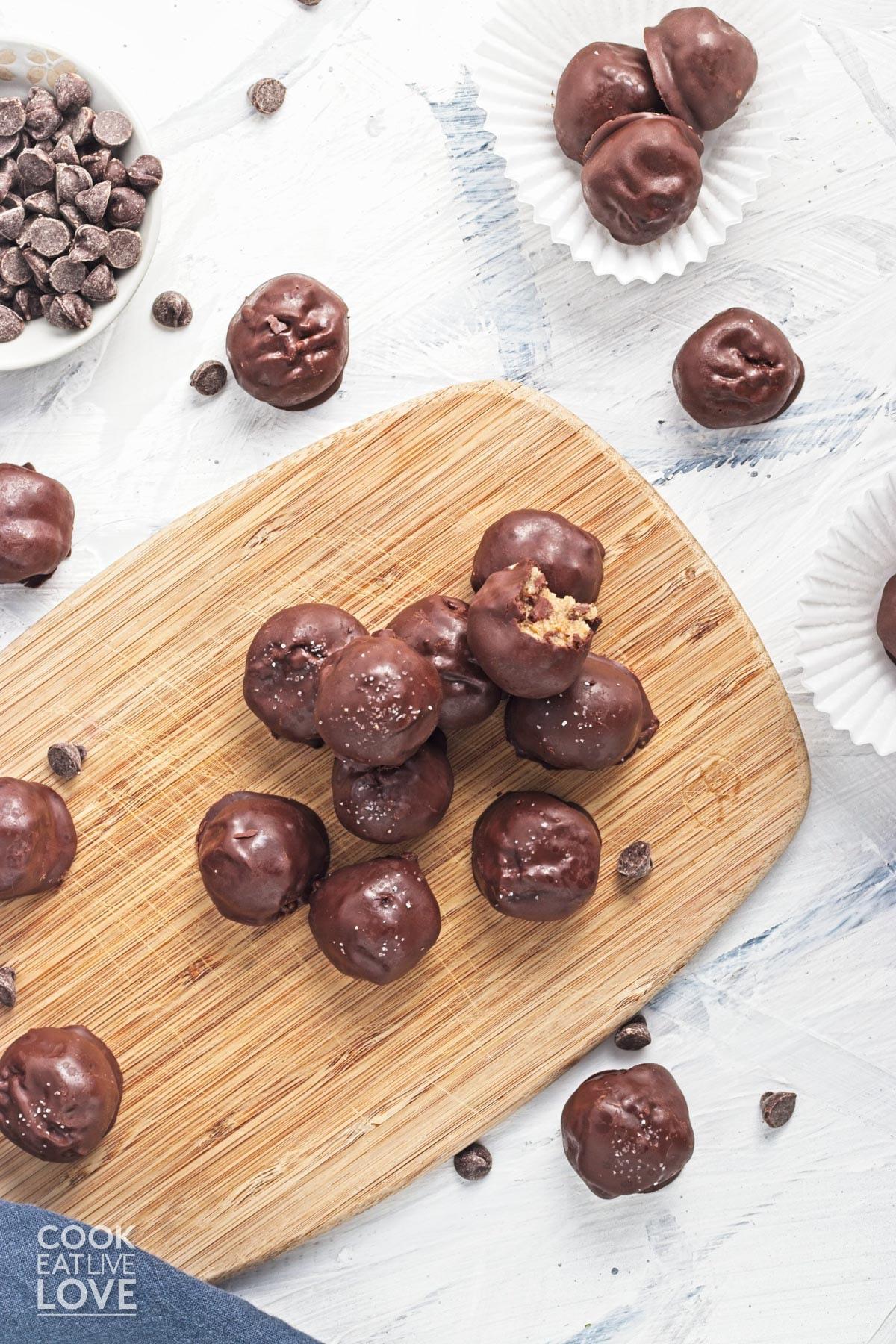 Cookie dough bites piled up on a wooden board and some scattered around. 