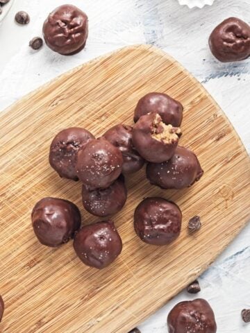 Cookie dough bites stacked on top of each other on a wooden baord on the table.