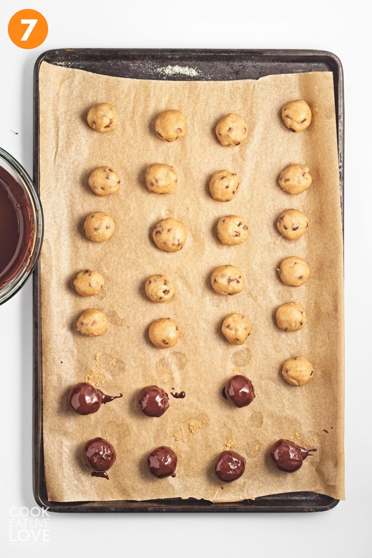 Cookie dough bites dipped in chocolate and some not laid out on a baking tray.