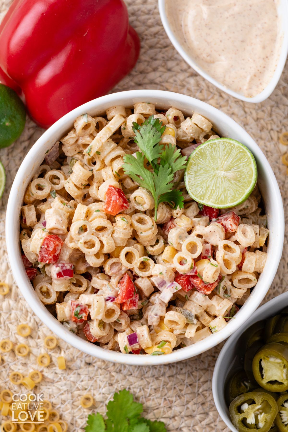 A bowl of Mexican macaroni salad on the table garnished with lime and cilantro.