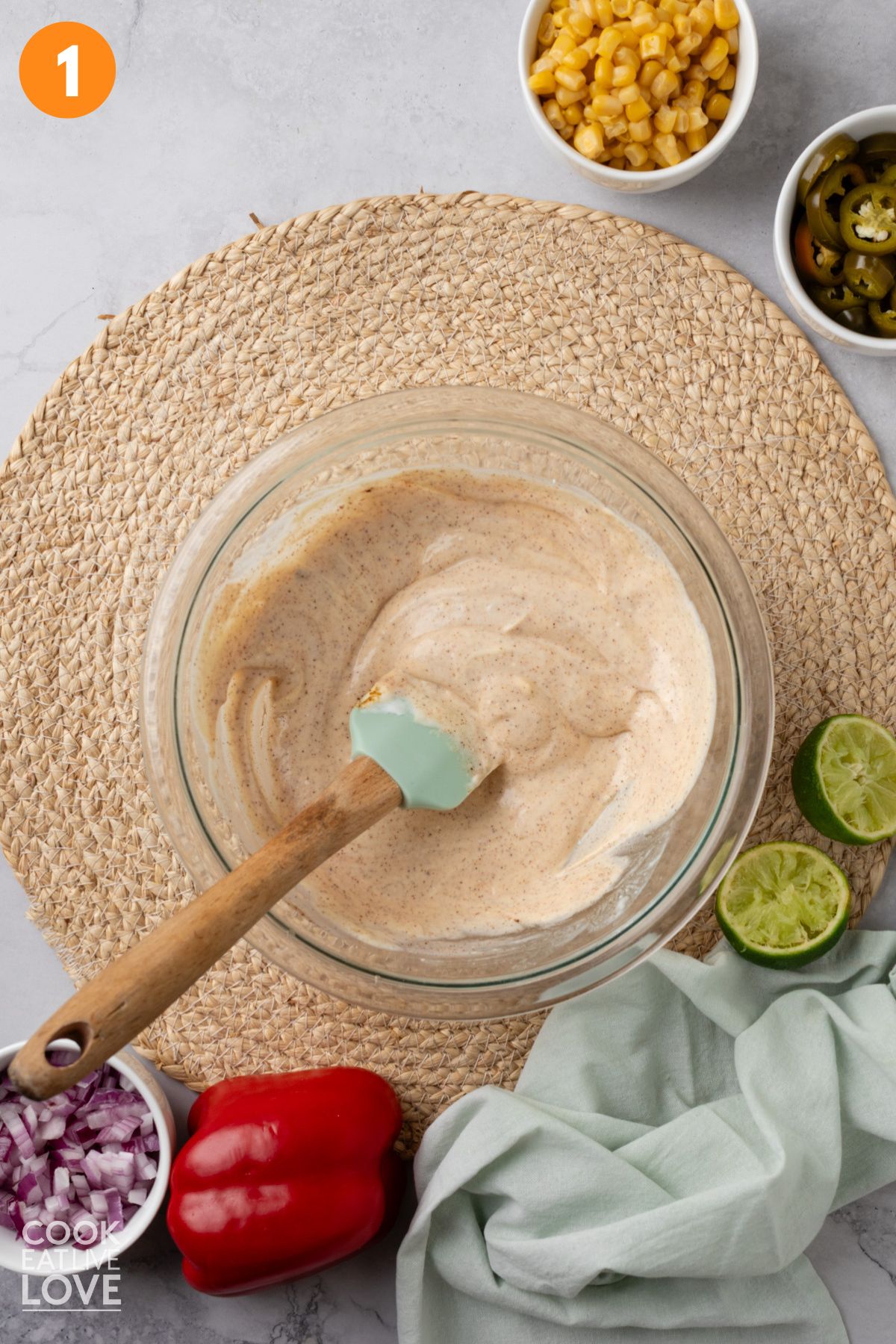 Mexican macaroni salad dressing mixed in a bowl with a spatula resting in it.