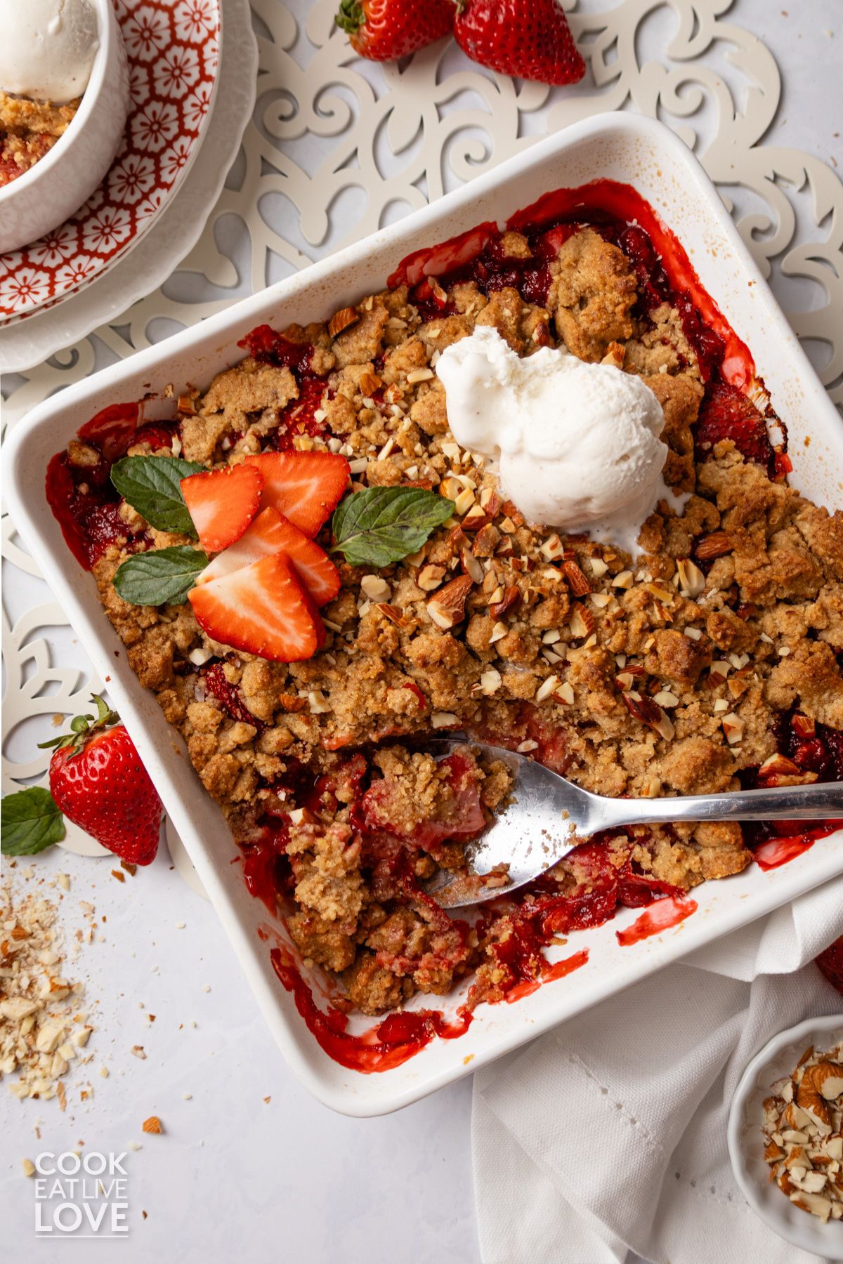Strawberry crumble in a white square baking dish with a spoon scooping some up.