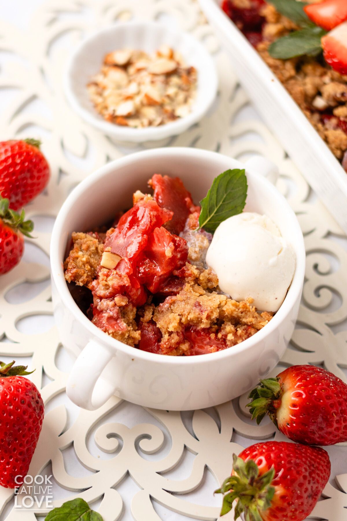 A bowl of strawberry crumble topped with ice cream and surrounded by fresh berries.