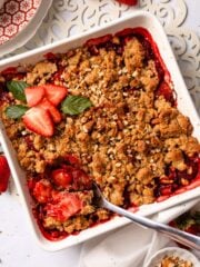 Strawberry crumble in a baking dish with a spoon resting in the corner.