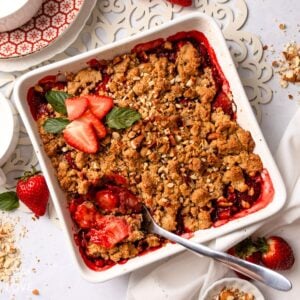 Strawberry crumble in a baking dish with a spoon resting in the corner.