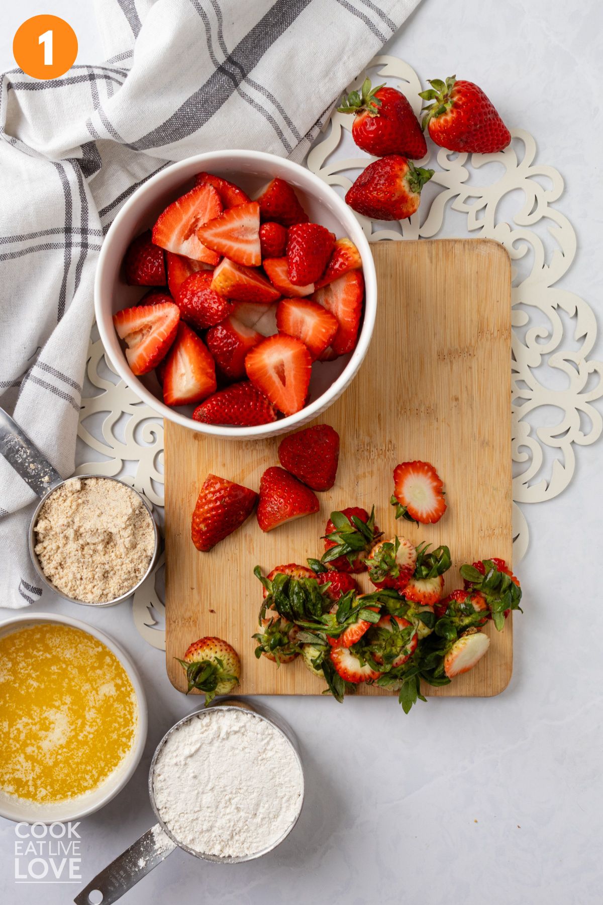 Strawberries cut in a bowl and the green tops on a cutting board.