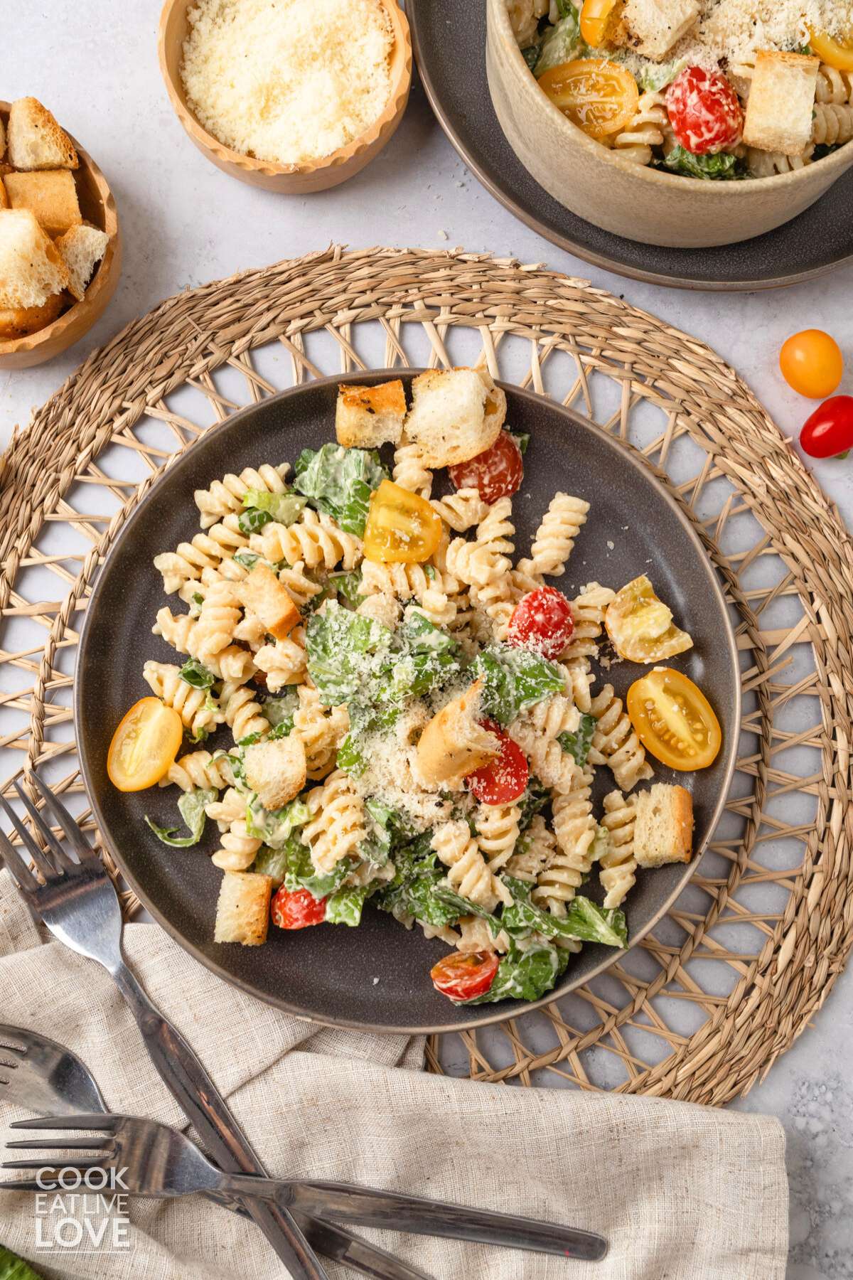 A plate of Caesar pasta salad on a table with a bowl of more in the corner.