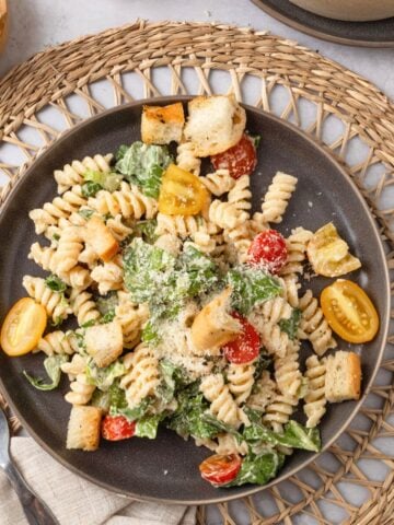 A plate of Caesar pasta salad on a woven mat on the table.