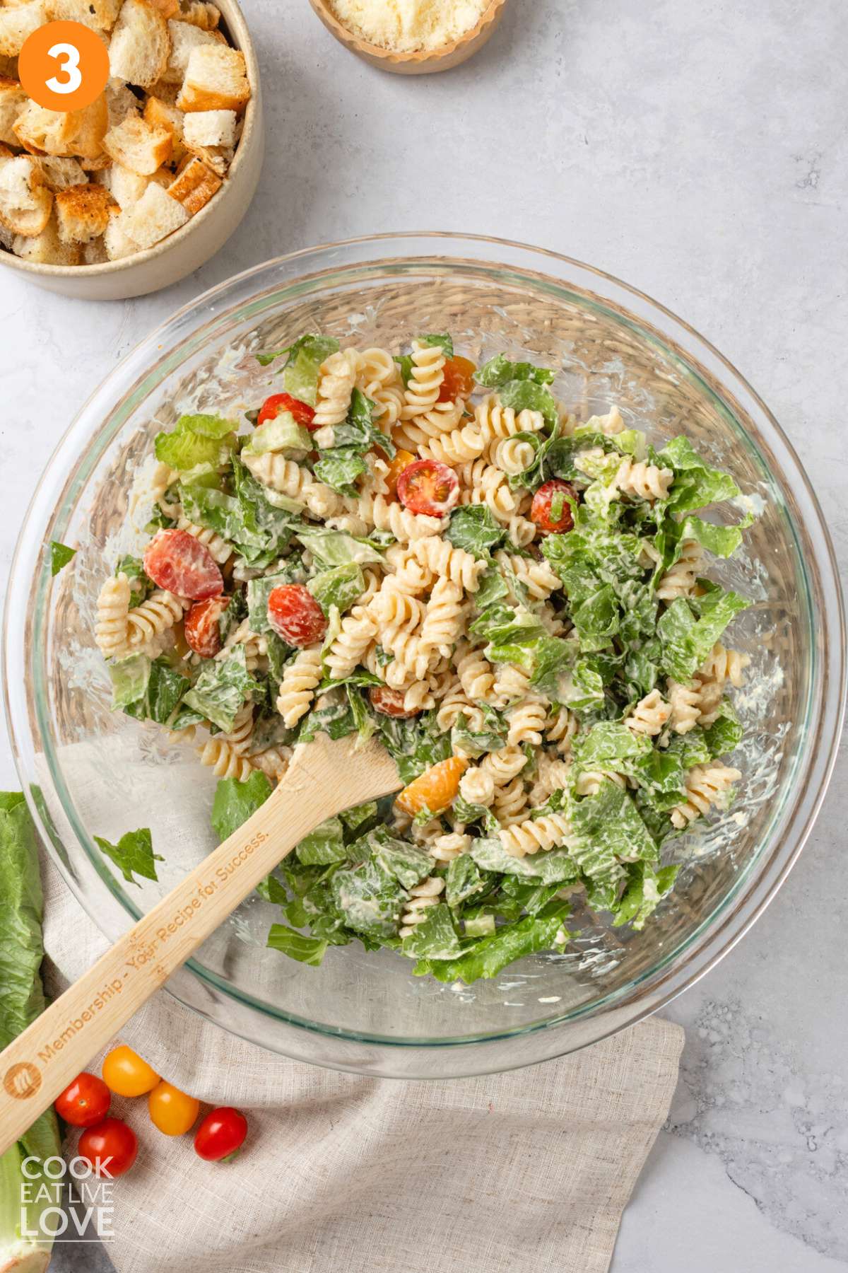 Caesar pasta salad mixed with the dressing and a wooden utensil in the bowl.