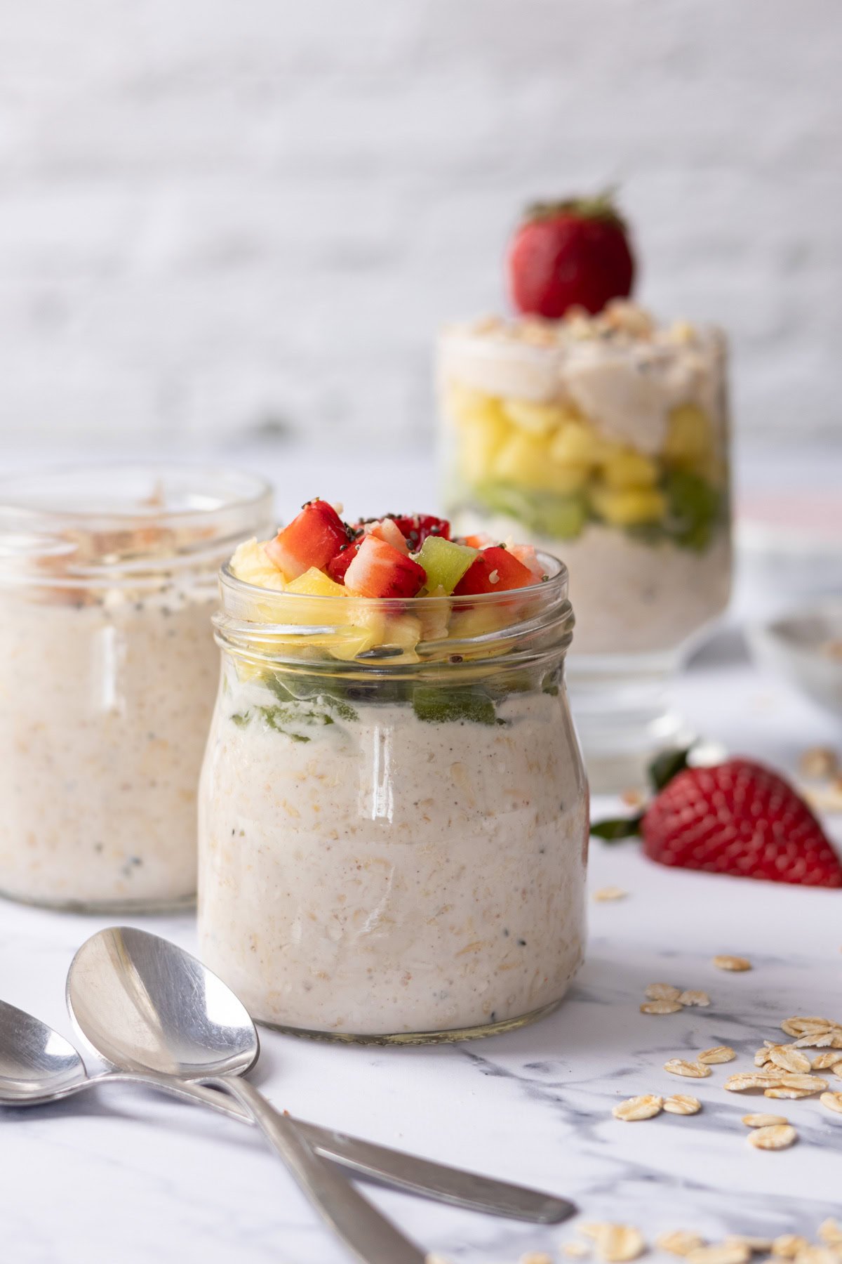 Greek yogurt overnight oats in jars on a table layered with fruit.