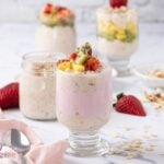 Greek yogurt overnight oats in a glass topped with fresh fruit and layered with pink yogurt.