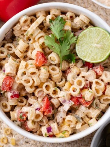 A bowl of Mexican macaroni salad garnished with a lime and cilantro.