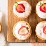 Mini strawberry tarts on a wooden board topped with sliced strawberry.