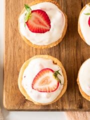 Mini strawberry tarts on a wooden board topped with sliced strawberry.