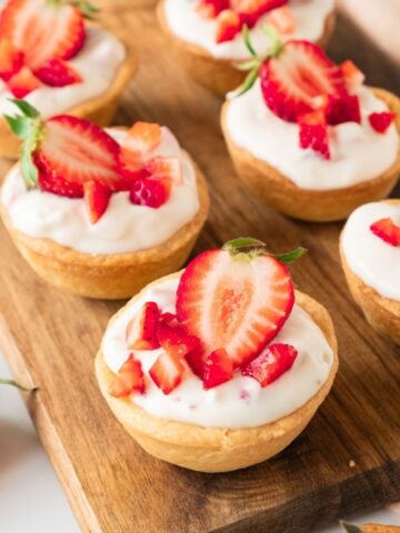 Mini strawberry tarlets on a wooden board with fresh strawberries on top and around.