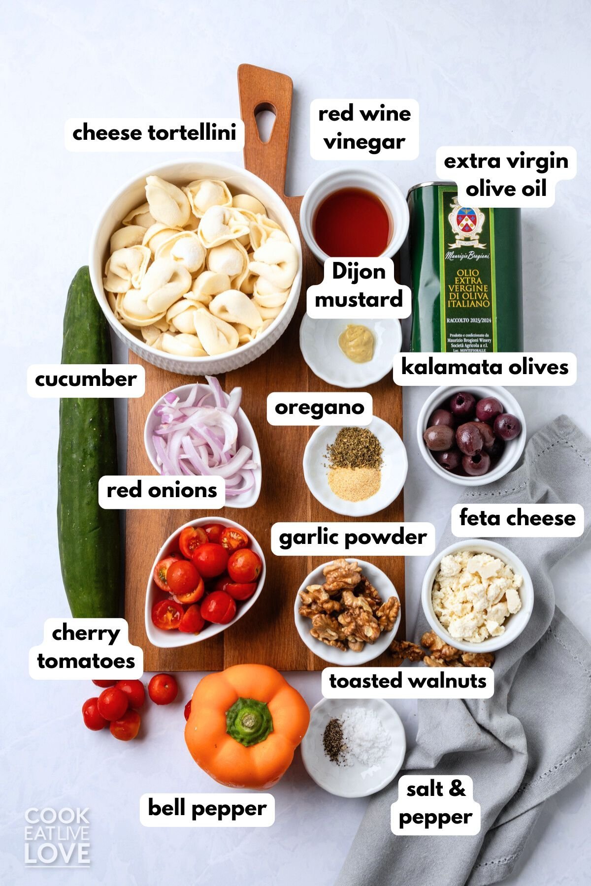 Ingredients to make a Greek tortellini salad on the table with labels to identify each one.