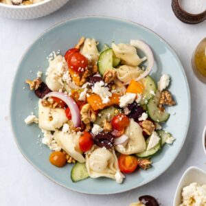 Greek tortellini salad on a plate with colorful vegetables, feta, and walnuts.
