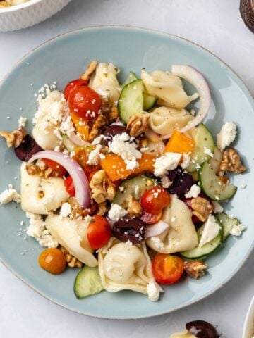 Greek tortellini salad on a plate with colorful vegetables, feta, and walnuts.