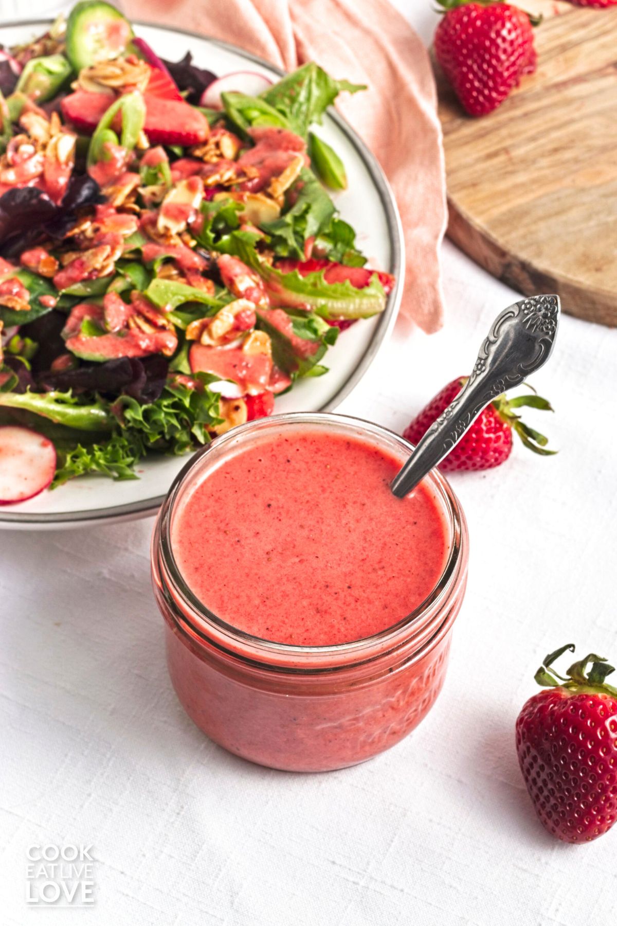 A jar of strawberry vinaigrette next to a salad on a plate.