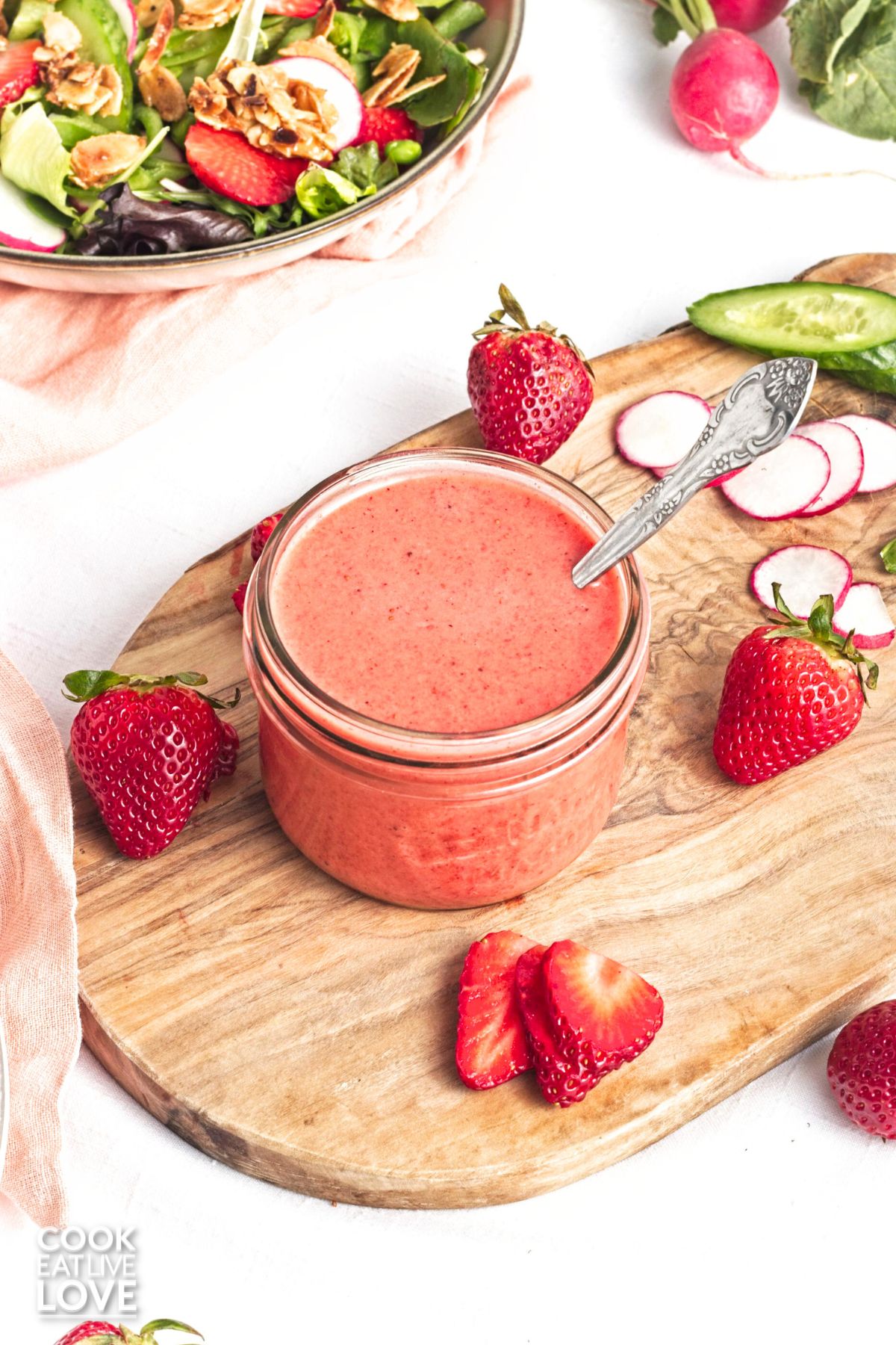 A small jar of strawberry vinaigrette on a wooden cutting board with fresh berries around it.