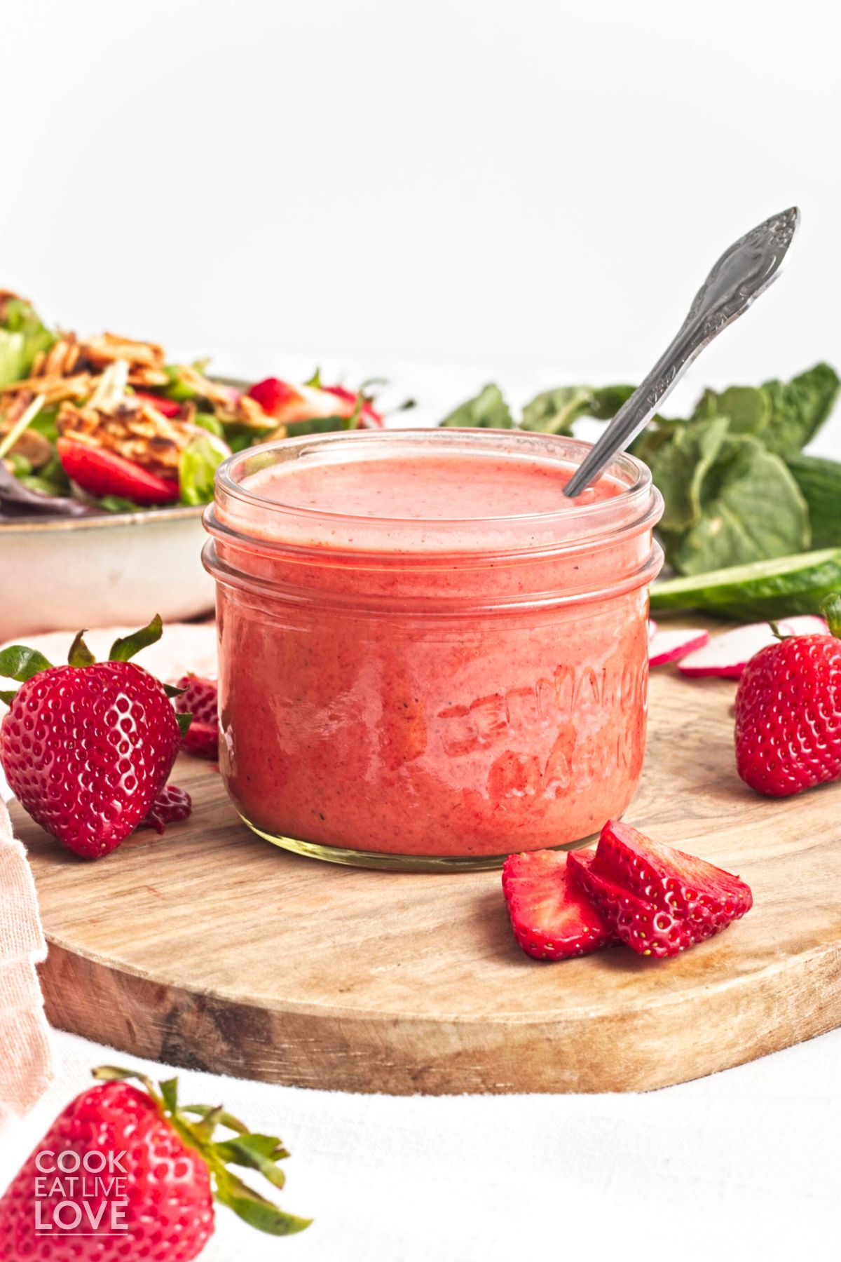 A jar of strawberry dressing with a spoon in it and fresh berries cut around it.