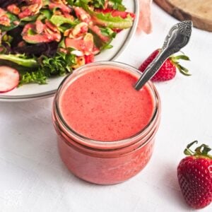 A small jar of strawberry vinaigrette with a spoon in the jar.