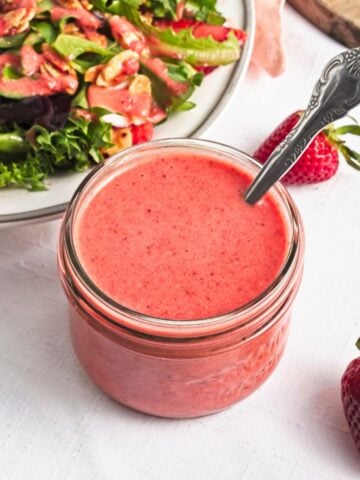 A small jar of strawberry vinaigrette with a spoon in the jar.