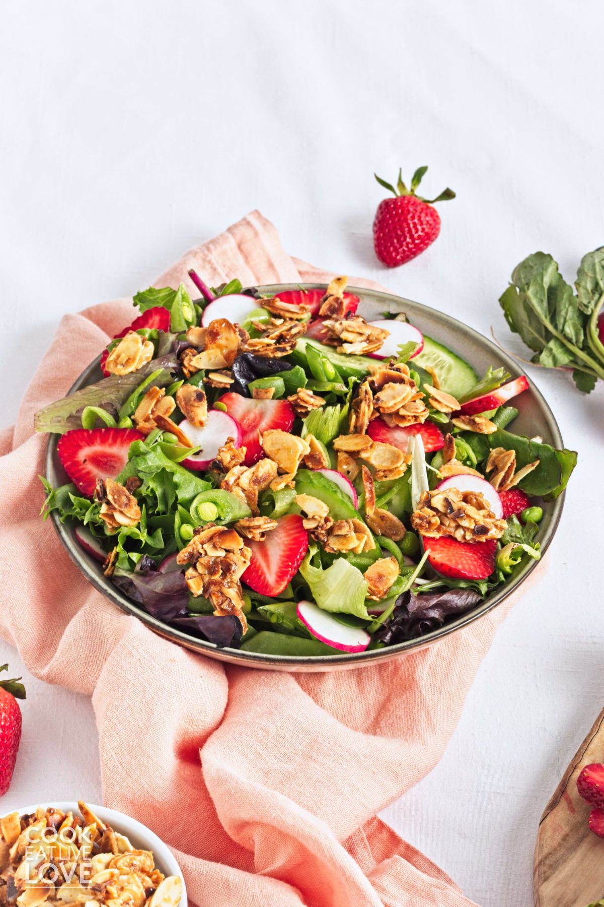 A bowl of strawberry salad on a table with a pink napkin to the side and whole berries.