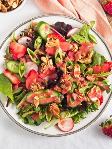 A summer strawberry salad on a white plate with fresh berries on the side.