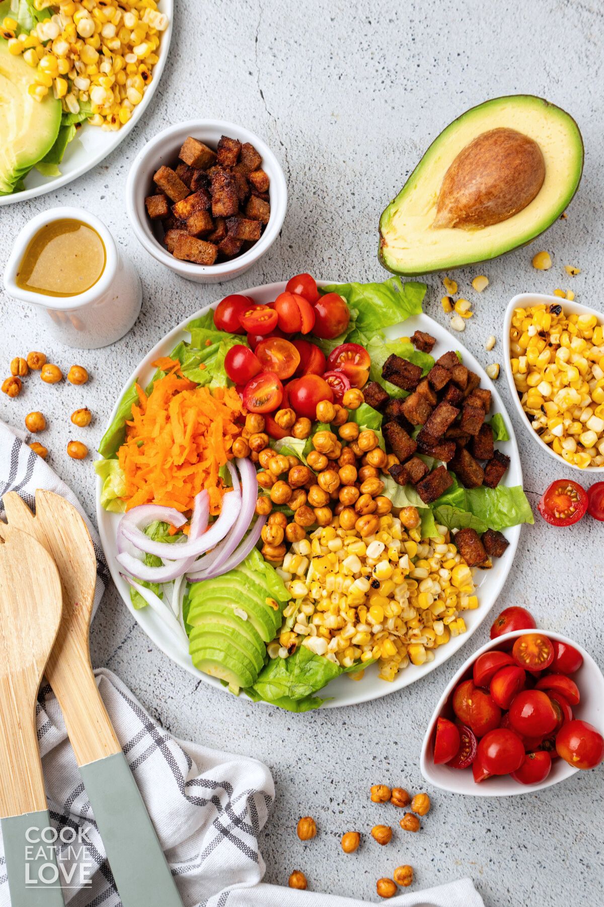 Vegan cobb salad on a white plate surrounded by bowls of ingredients and serving utensils.