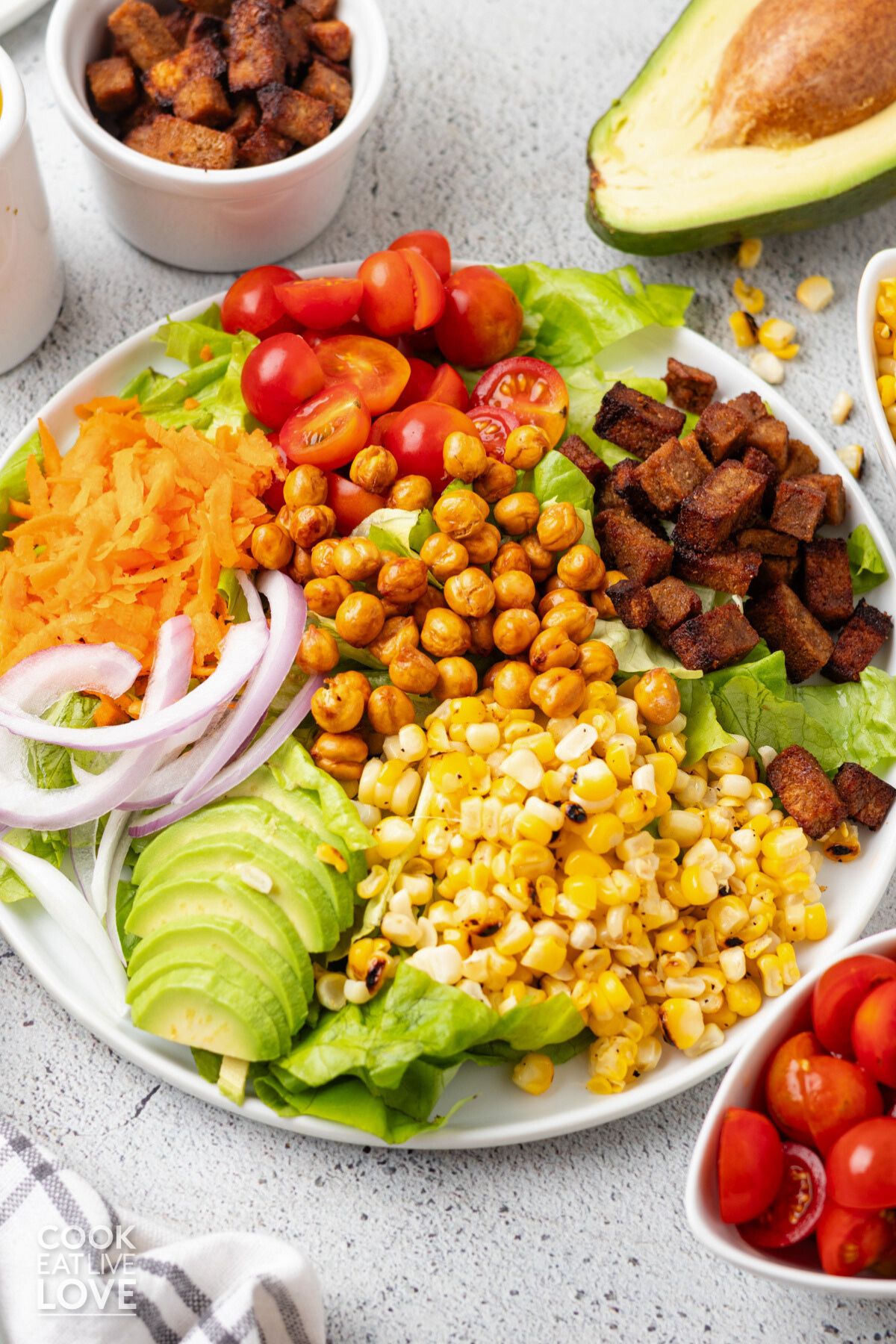 Vegan cobb salad on a plate with corn, chickpeas, tofu, and vegetables in separate piles on top of lettuce.