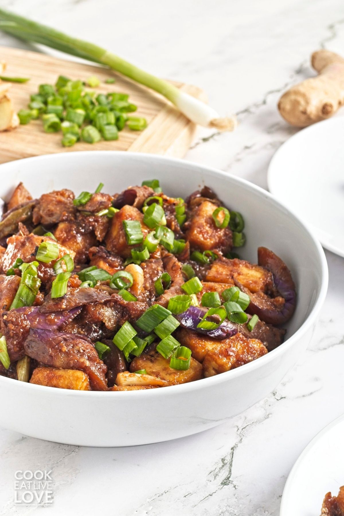 A bowl of eggplant tofu stir fry on a table garnished with green onions.