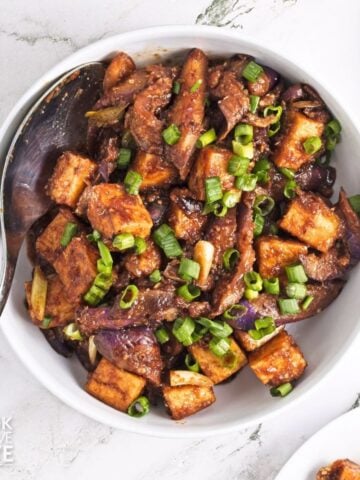 Eggplant tofu recipe served up in a white bowl and topped with sliced green onions.