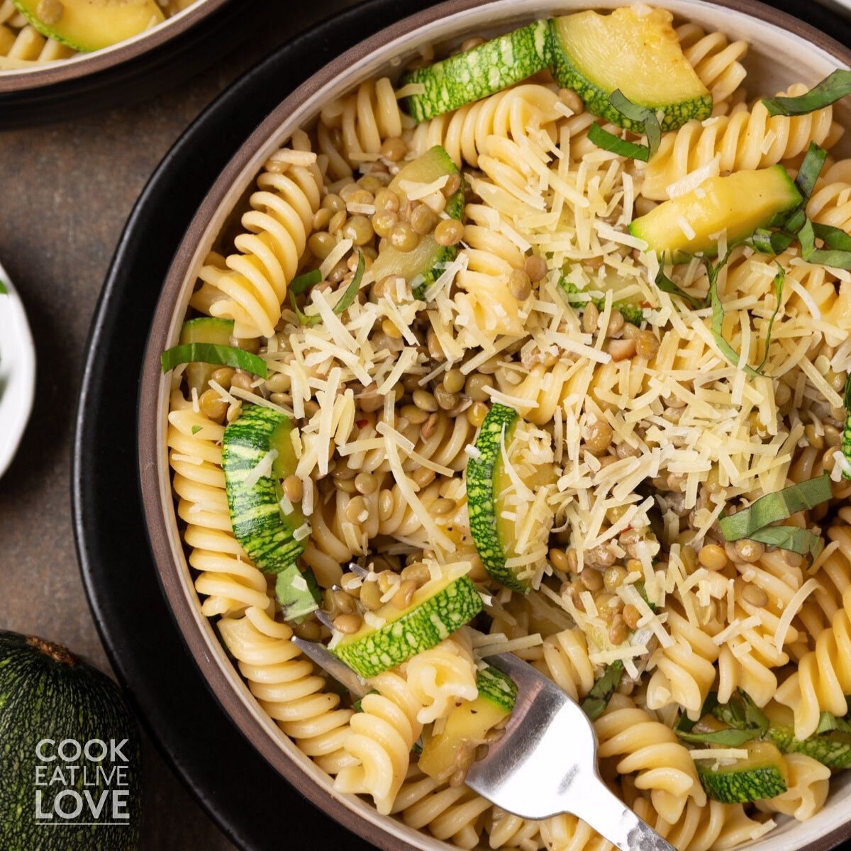 A bowl of lentil zucchini pasta with a fork resting in the side.