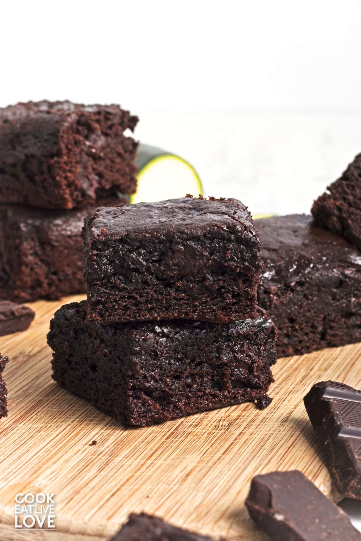 Two vegan zucchini brownies stacked up in front of more on a wooden board.