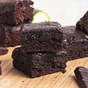Two zucchini brownies stacked and in front of more scattered around on a table.
