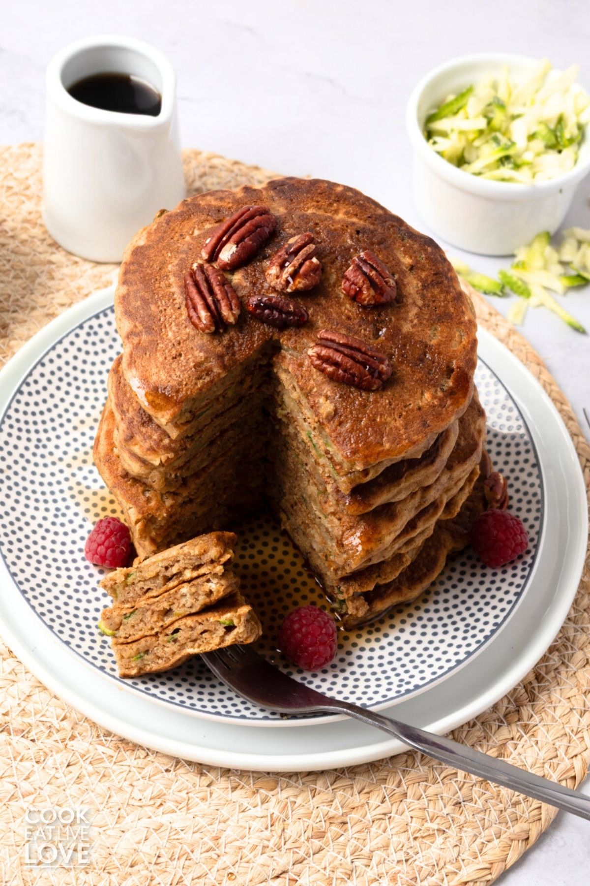 A stack of zucchini pancakes with a portion cut and on a fork in the front.
