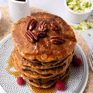 A stack of zucchini pancakes on a plate drizzled with maple syrup.