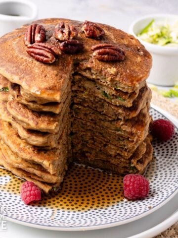 A stack of five zucchini pancakes with a triangle cut from the whole stack to show the inside.