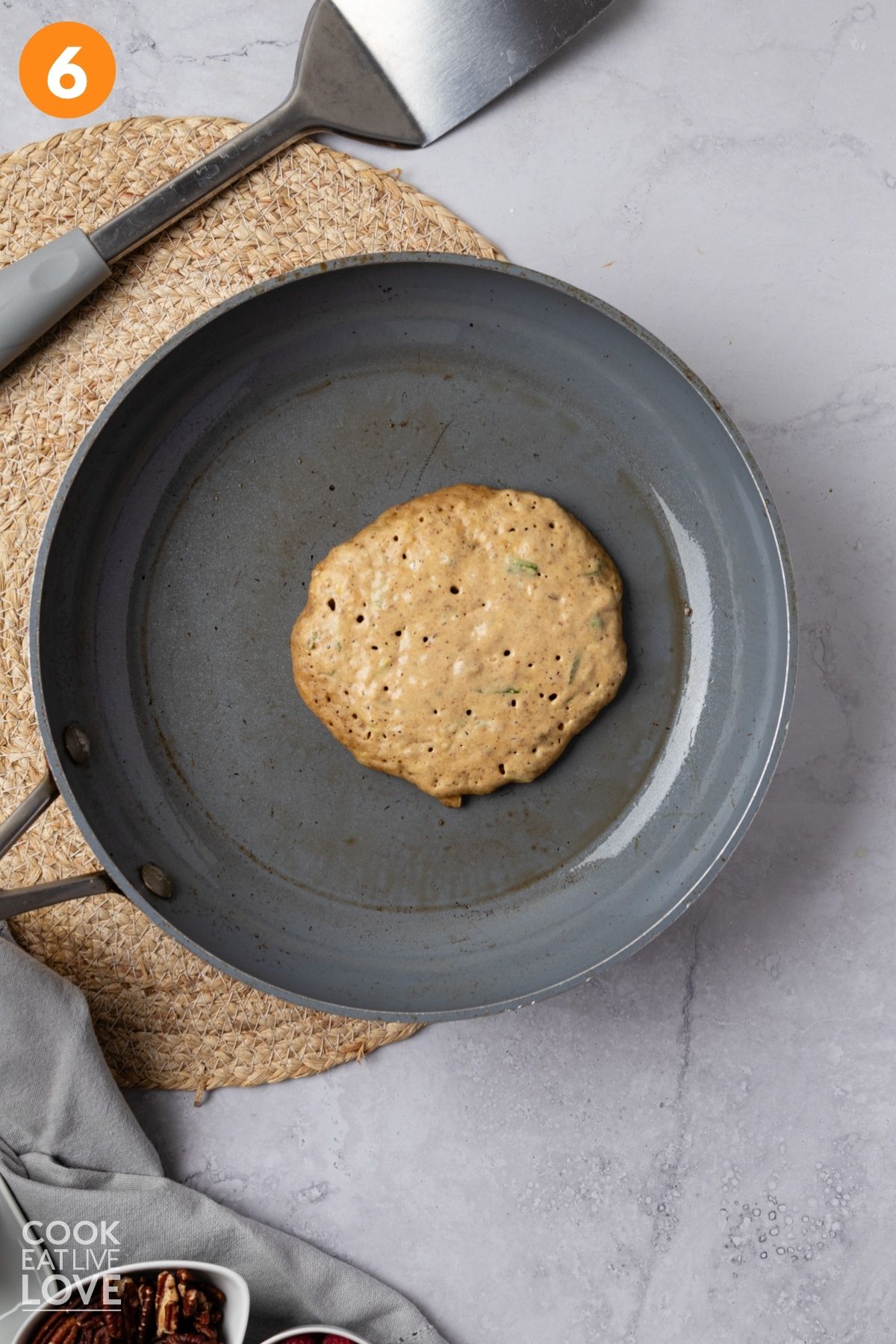Zucchini pancake cooking in a skillet.